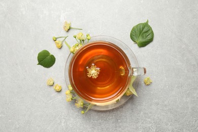 Cup of tea and linden blossom on light grey table, flat lay