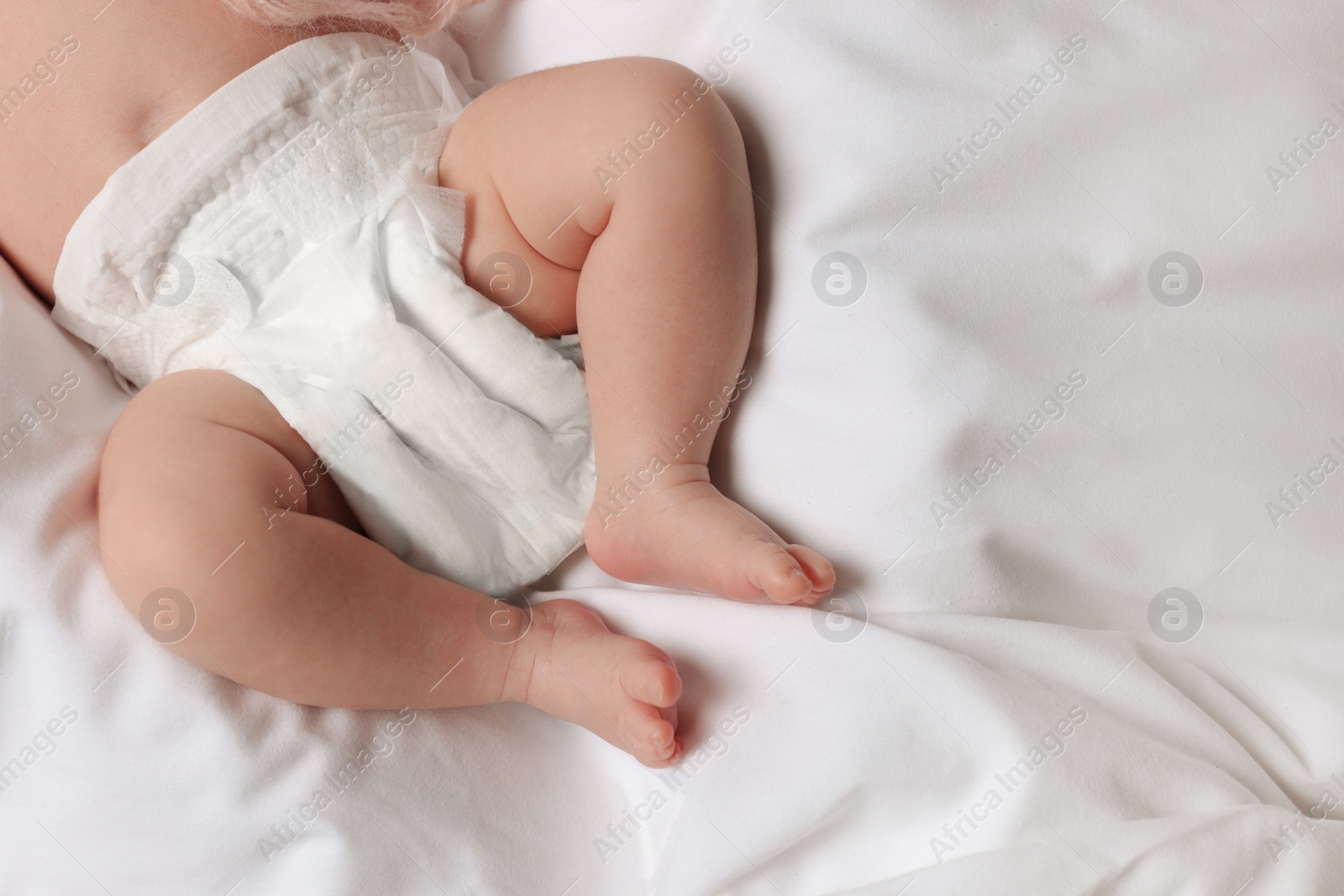 Photo of Little baby in diaper lying on soft bed, top view. Space for text