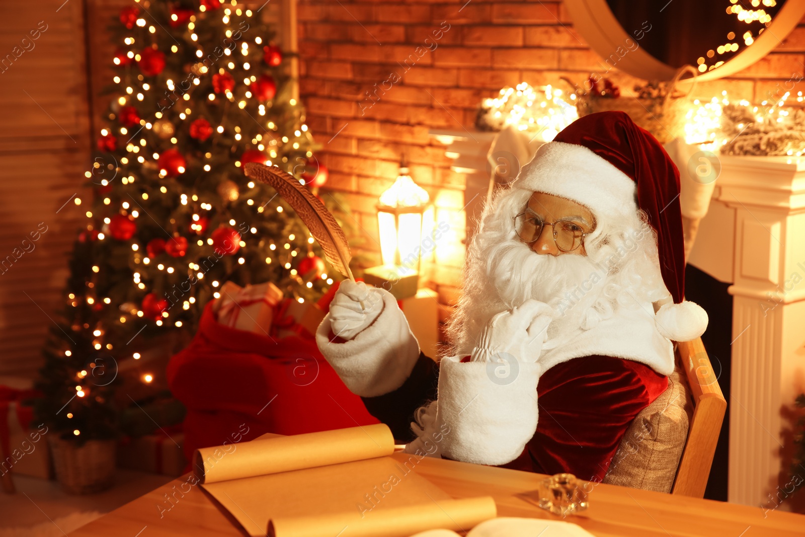 Photo of Santa Claus with wish list at table indoors