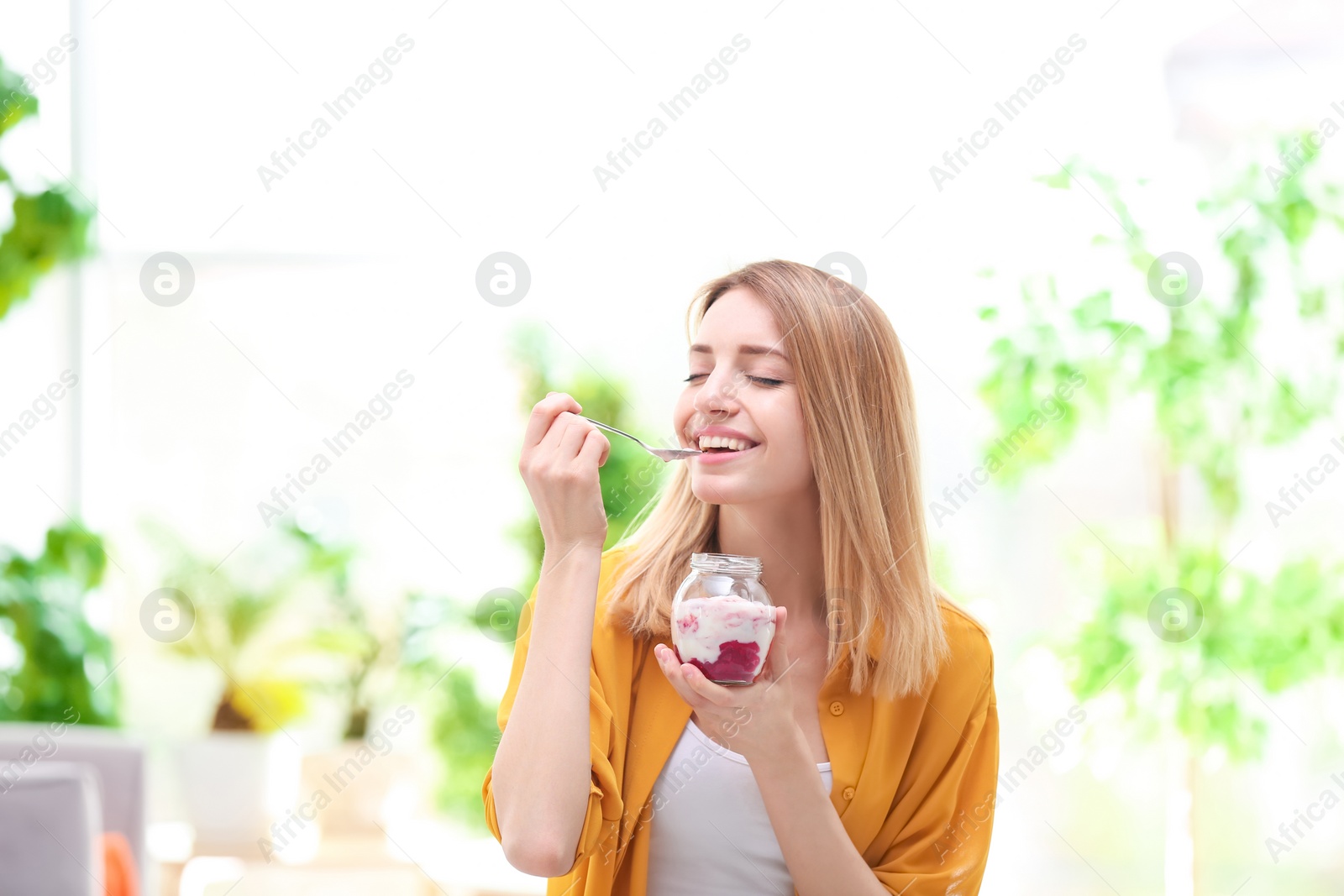 Photo of Young attractive woman eating tasty yogurt, indoors