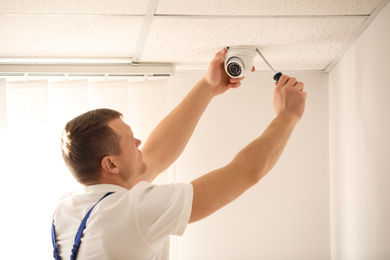 Technician installing CCTV camera on ceiling indoors