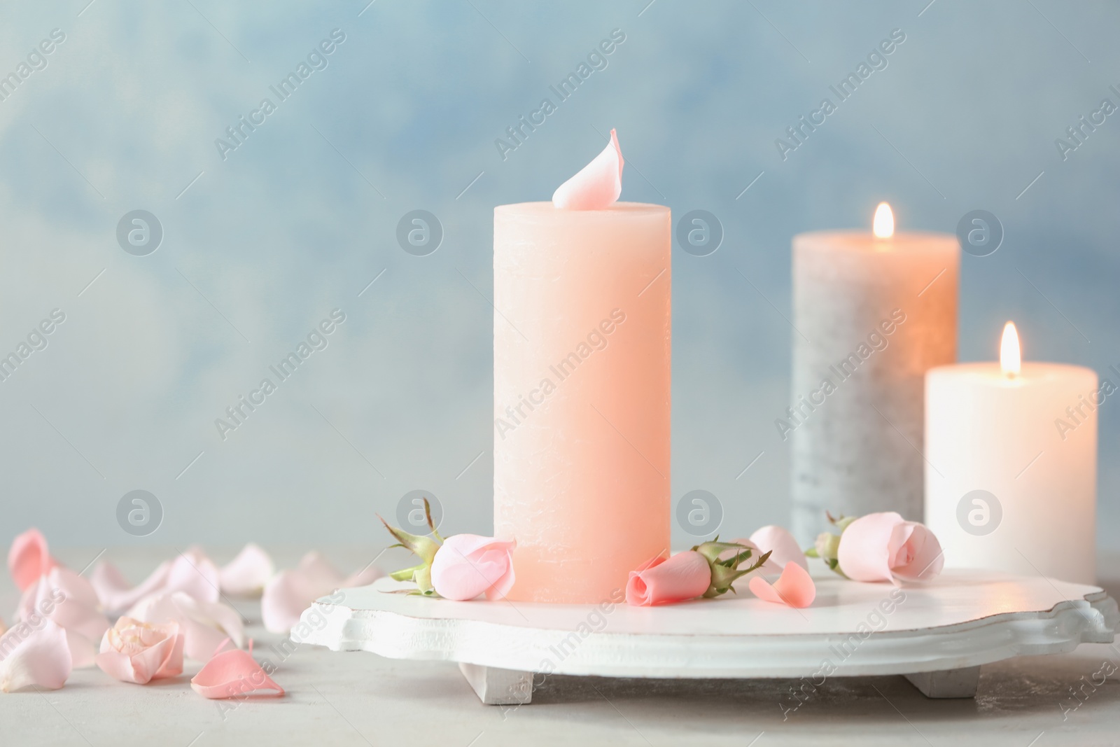 Photo of Candles with floral decor on table against color background