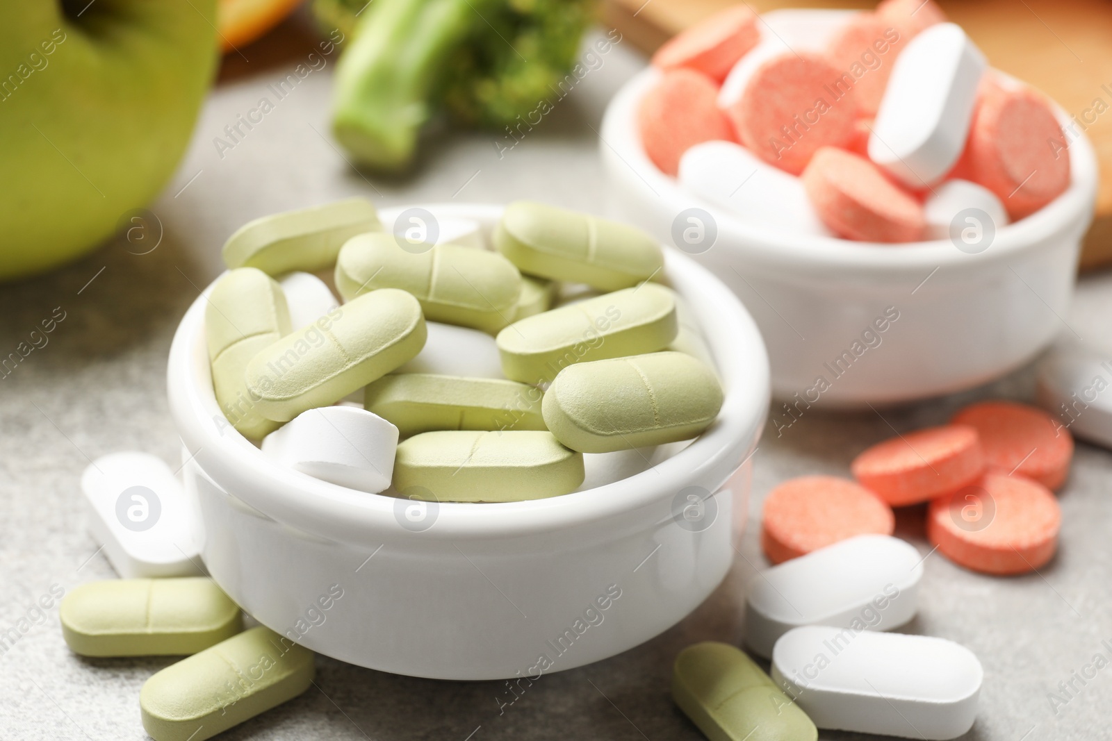 Photo of Dietary supplements. Different pills in bowls on grey table, closeup