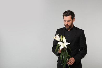 Sad man with white lilies mourning on light grey background, space for text. Funeral ceremony