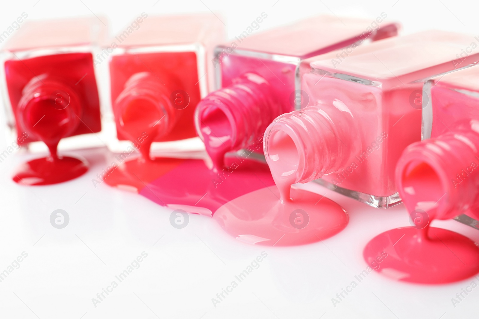 Photo of Spilled different nail polishes with bottles on white background, closeup