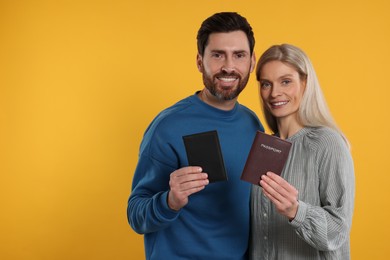 Immigration. Happy man and woman with passports on orange background, space for text