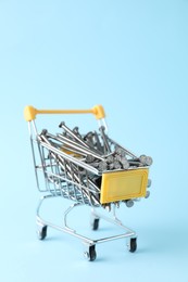 Photo of Metal nails in shopping cart on light blue background. closeup