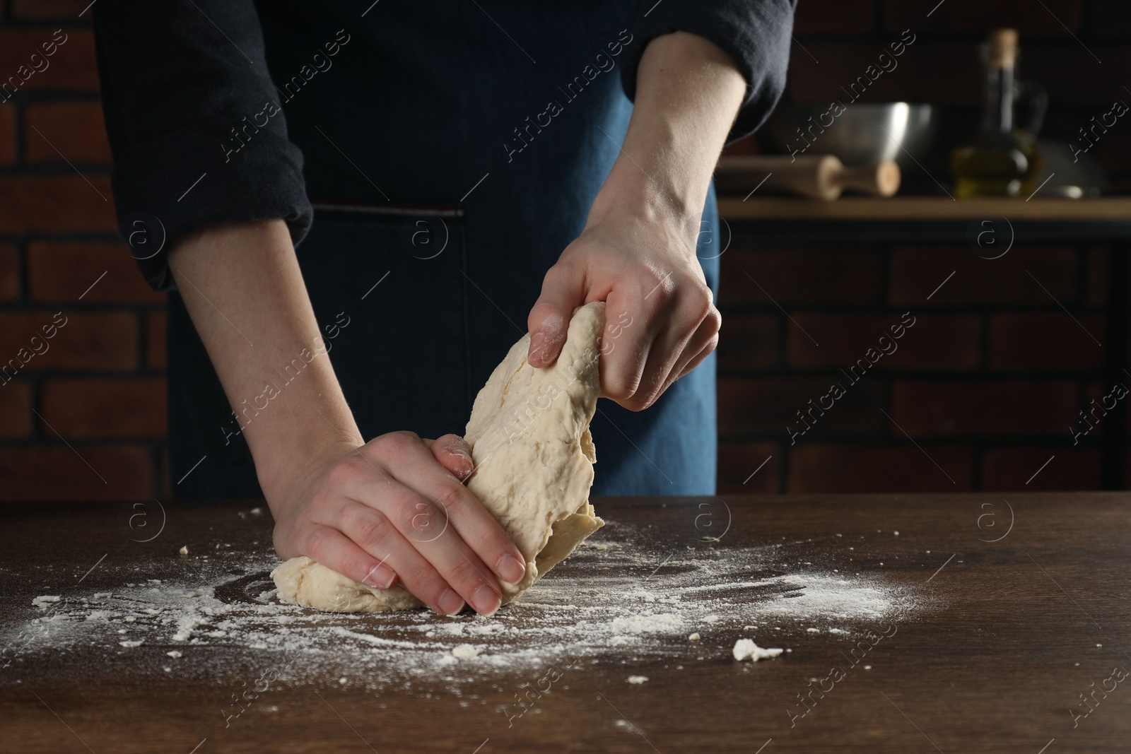 Photo of Making bread. Woman kneading dough at wooden table in kitchen, closeup