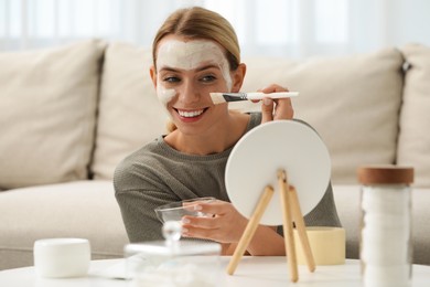 Photo of Young woman applying face mask in frontmirror at home. Spa treatments