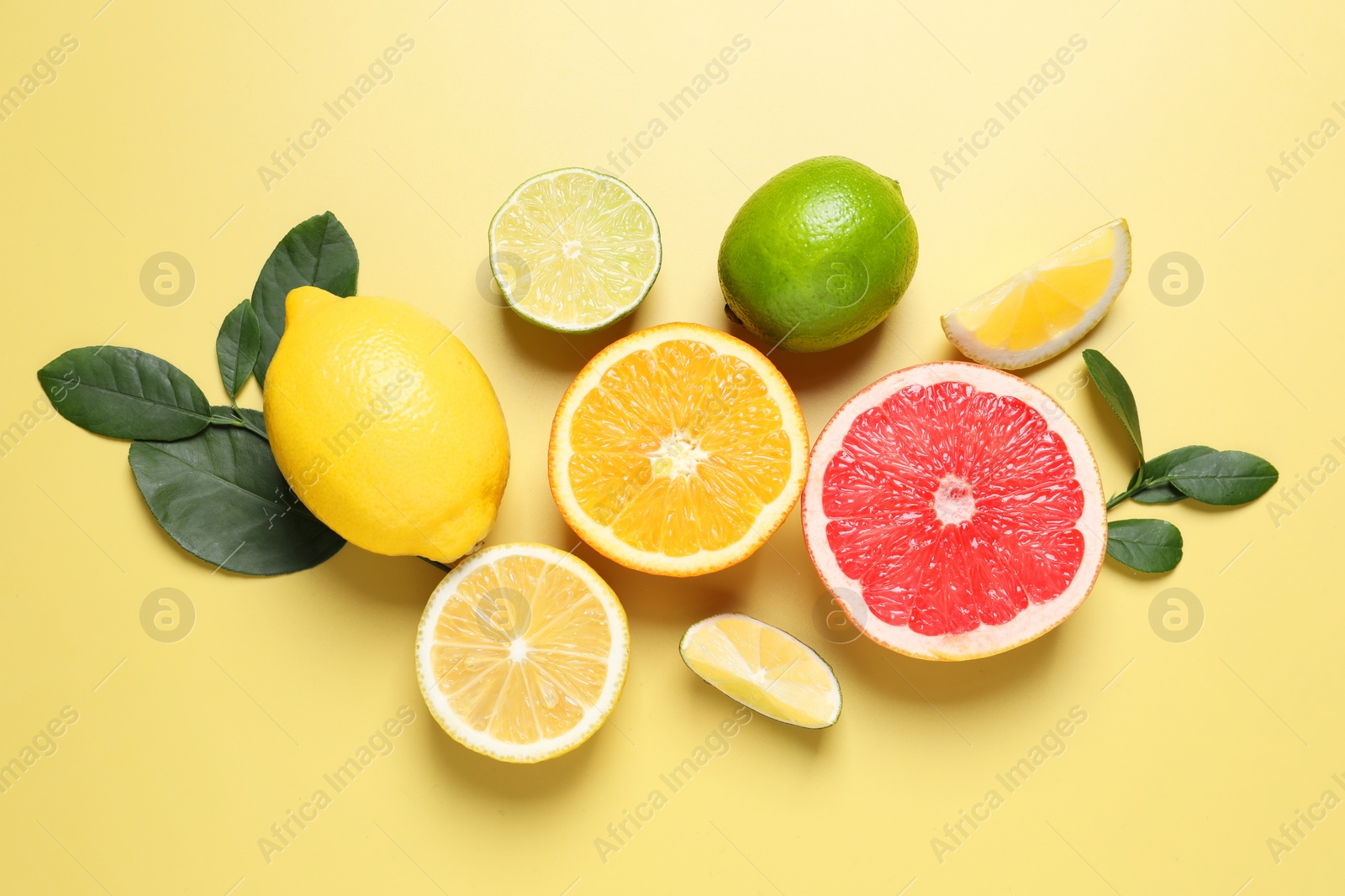 Photo of Different cut and whole citrus fruits on yellow table, flat lay