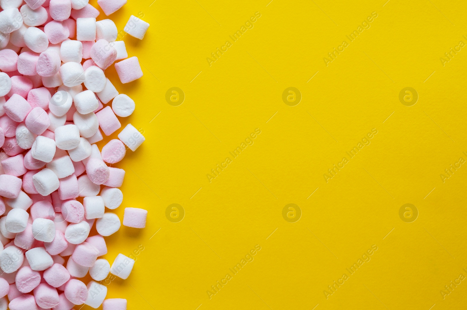 Photo of Delicious puffy marshmallows on yellow background, flat lay. Space for text