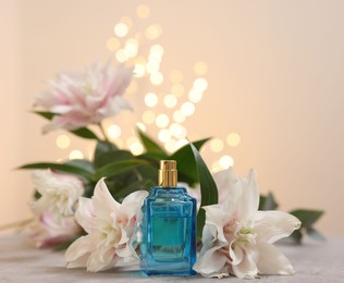 Photo of Bottle of perfume and beautiful lily flowers on table against beige background with blurred lights, closeup