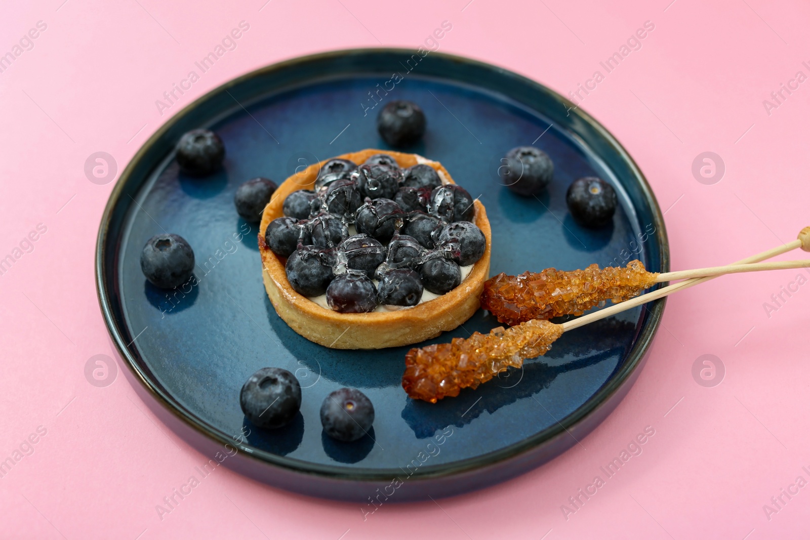 Photo of Plate with delicious cake, blueberries and sticks of sugar crystals on pink background. Food photography