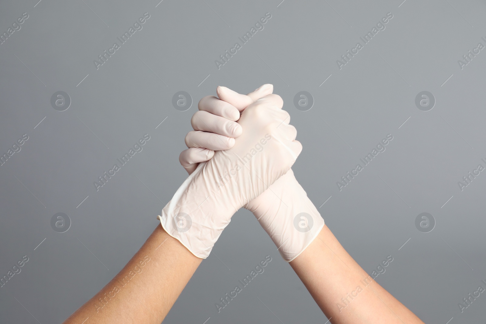 Photo of Doctors in medical gloves shaking hands on grey background, closeup