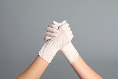 Doctors in medical gloves shaking hands on grey background, closeup