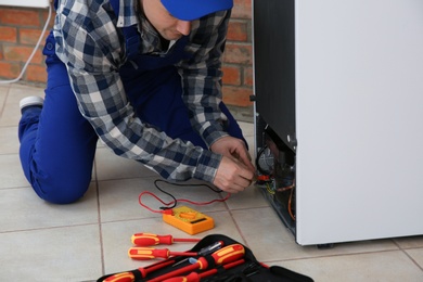 Male technician repairing broken refrigerator indoors, closeup