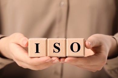 Photo of Woman holding wooden cubes with abbreviation ISO, closeup