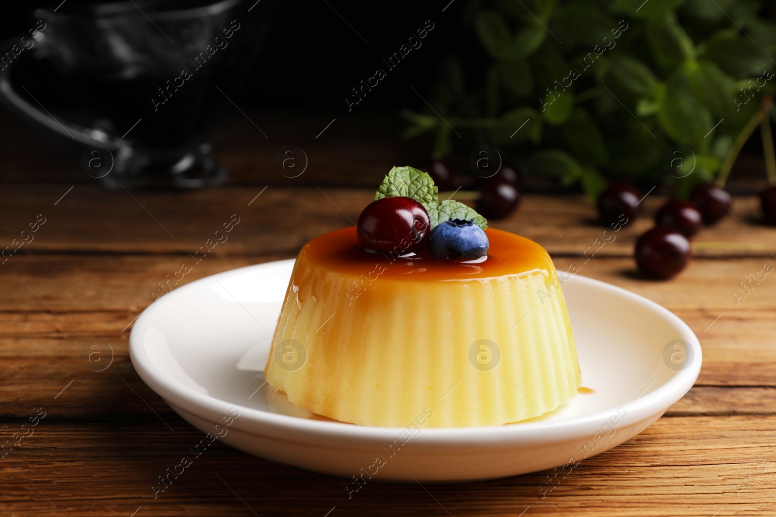 Photo of Plate of delicious caramel pudding with blueberry, cherry and mint on wooden table