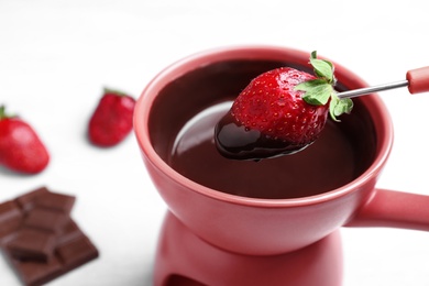 Photo of Dipping strawberry into pot with chocolate fondue on table, closeup