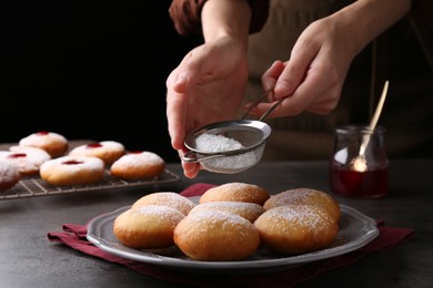 Photo of Woman dusting powdered sugar onto delicious Hanukkah donuts on grey table, closeup