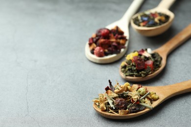 Photo of Different kinds of dry herbal tea in wooden spoons on light grey table, closeup. Space for text