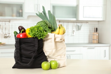 Textile shopping bags full of vegetables and fruits on table in kitchen. Space for text
