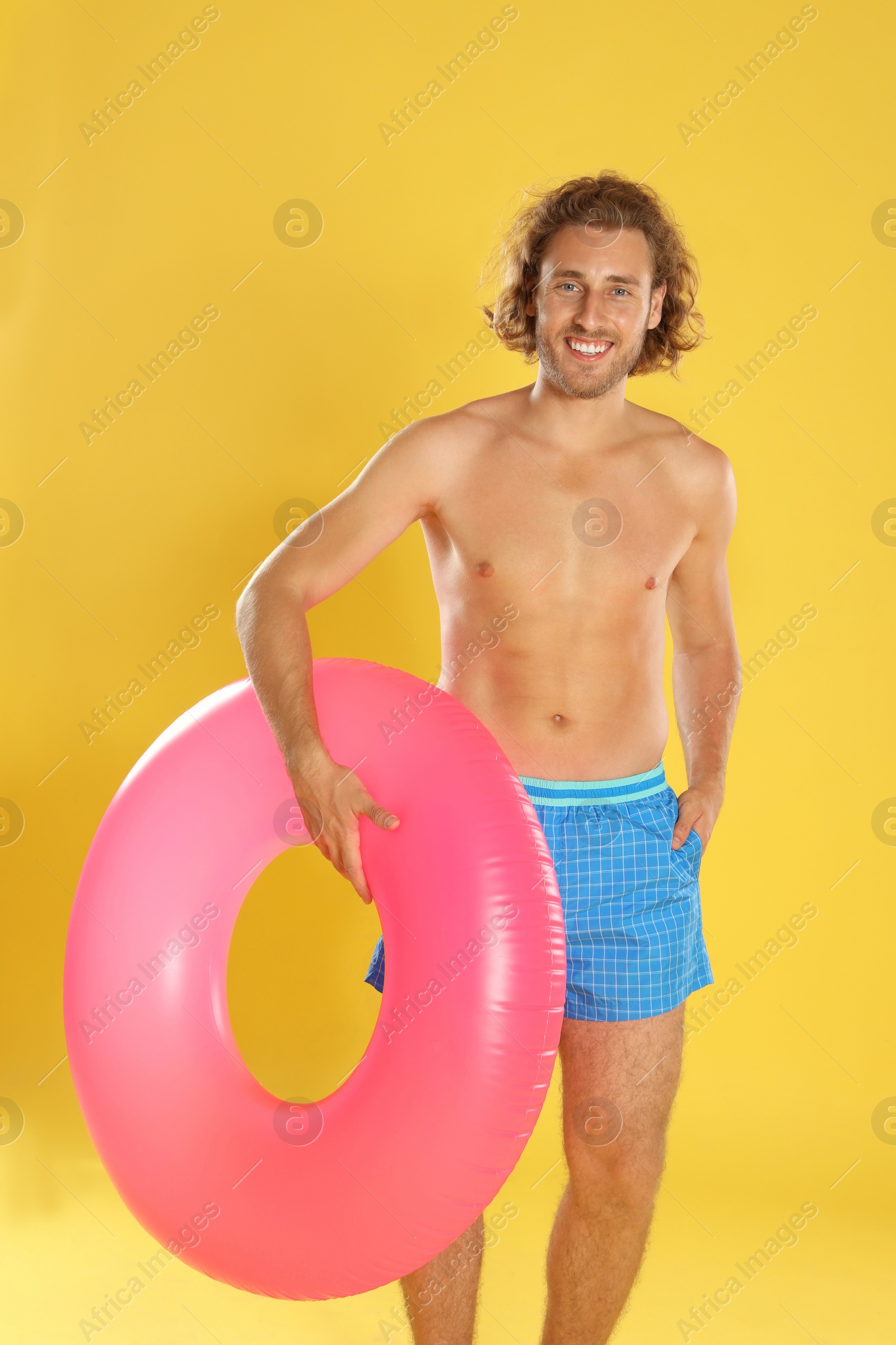 Photo of Attractive young man in beachwear with pink inflatable ring on yellow background