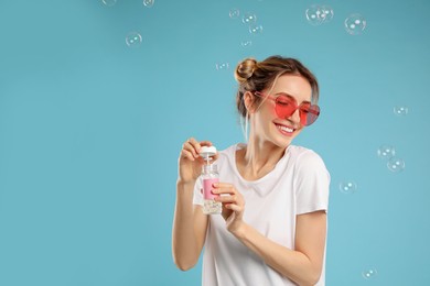 Young woman blowing soap bubbles on light blue background, space for text