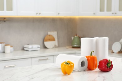 Photo of Rolls of paper towels and fresh ripe peppers on white marble table in kitchen. Space for text