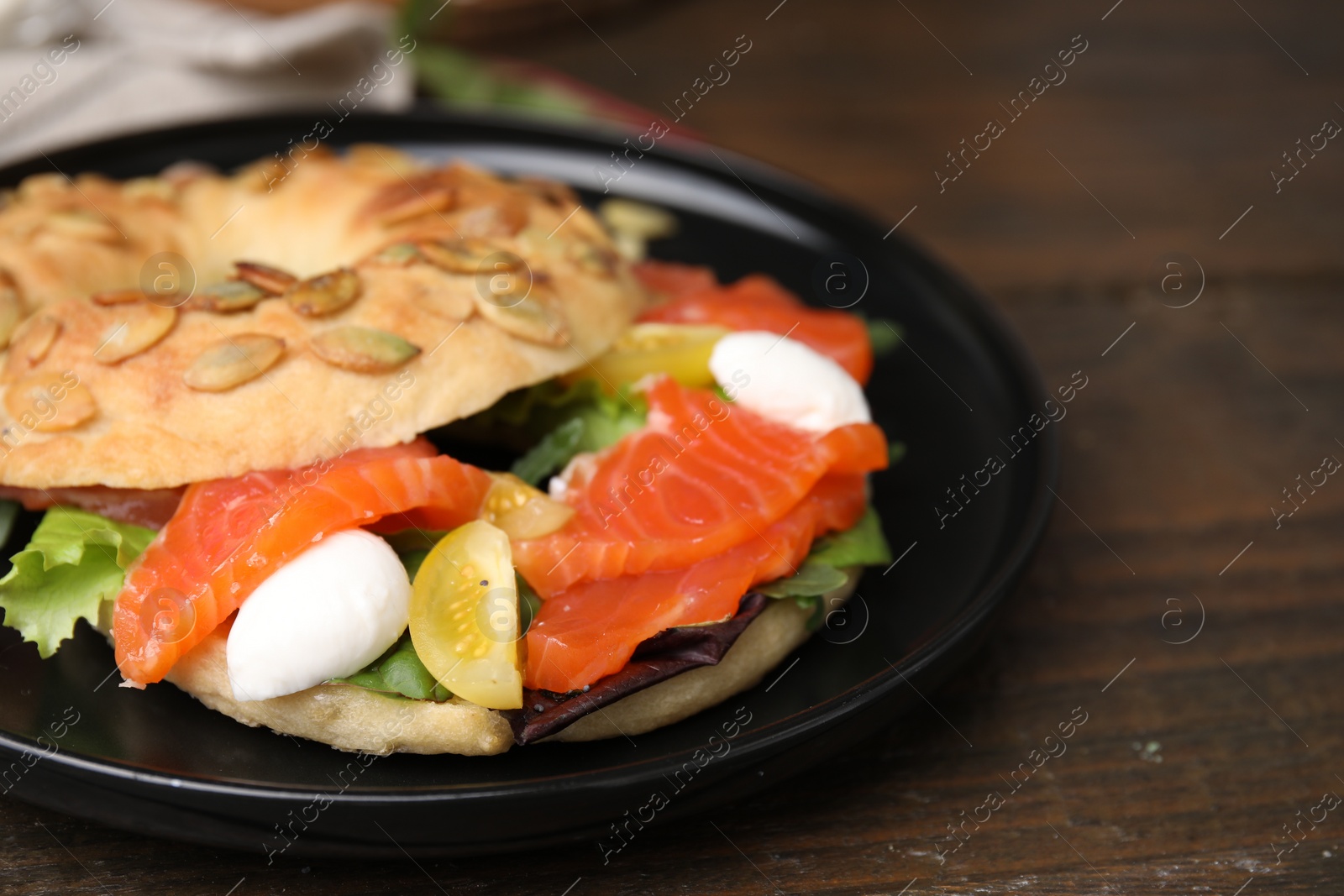 Photo of Tasty bagel with salmon, mozzarella cheese, tomatoes and lettuce on wooden table, closeup