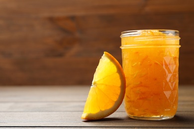 Photo of Delicious orange marmalade and citrus fruit slice on wooden table, closeup. Space for text