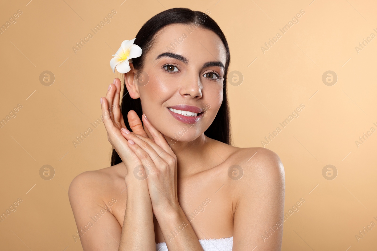 Photo of Young woman with plumeria flower in hair on beige background. Spa treatment