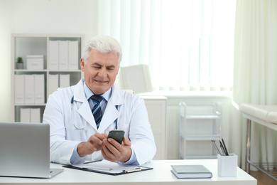 Photo of Senior doctor with smartphone at table in office