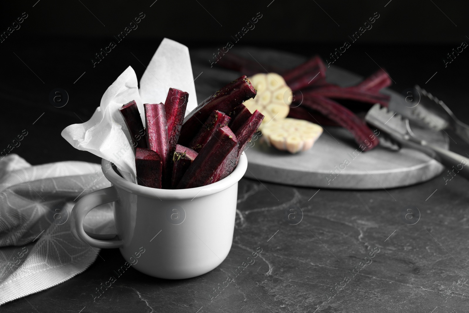 Photo of Tasty cut black carrot in cup on black slate table