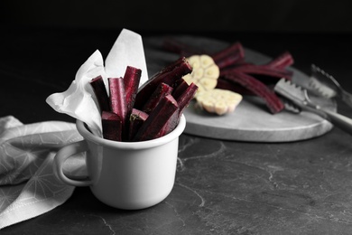 Tasty cut black carrot in cup on black slate table