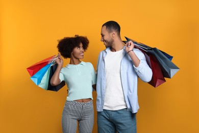 Happy African American couple with shopping bags on orange background