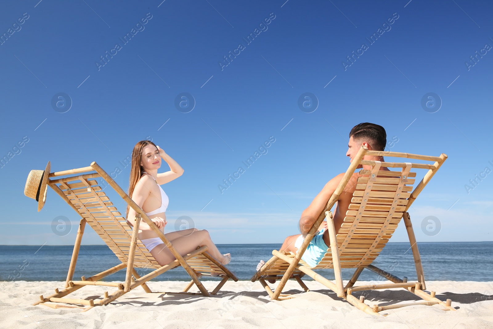 Photo of Woman in bikini and her boyfriend on deck chairs at beach. Happy couple