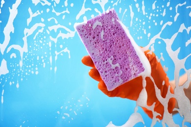 Photo of Woman cleaning glass with sponge against color background