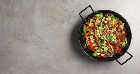 Photo of Stir-fry. Tasty noodles with meat and vegetables in wok on grey textured table, top view. Space for text