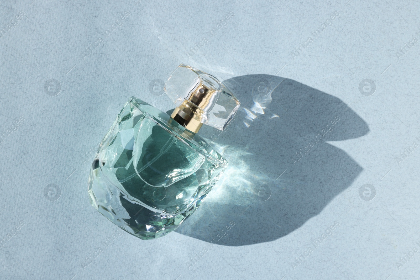 Photo of Luxury women's perfume. Sunlit glass bottle on grey background, top view. Space for text