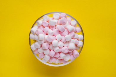 Photo of Bowl of delicious puffy marshmallows on yellow background, top view