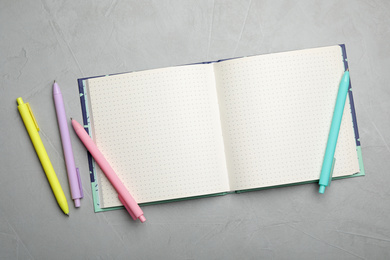 Stylish open notebook and pens on light grey table, flat lay