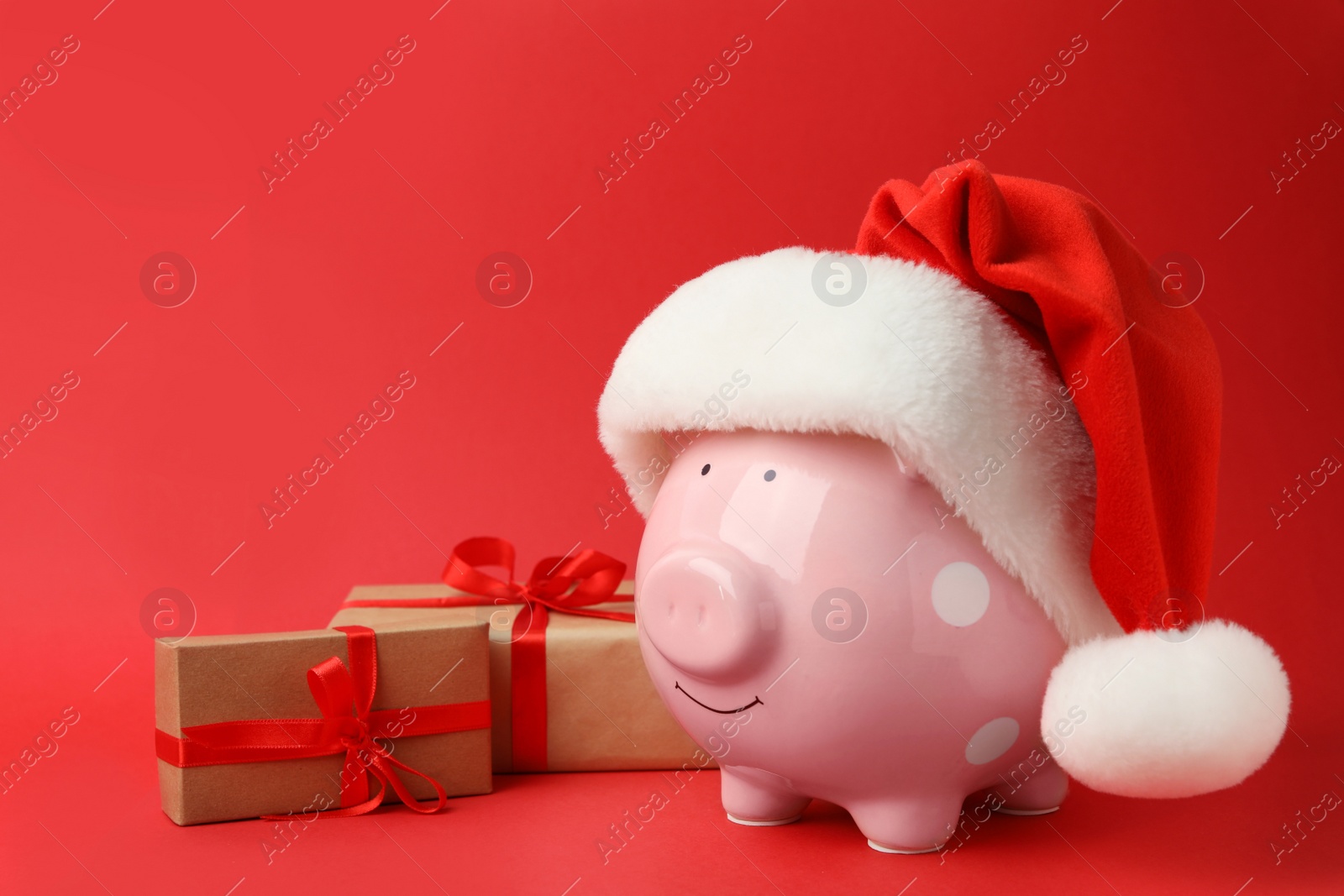 Photo of Piggy bank with Santa hat and gift boxes on red background