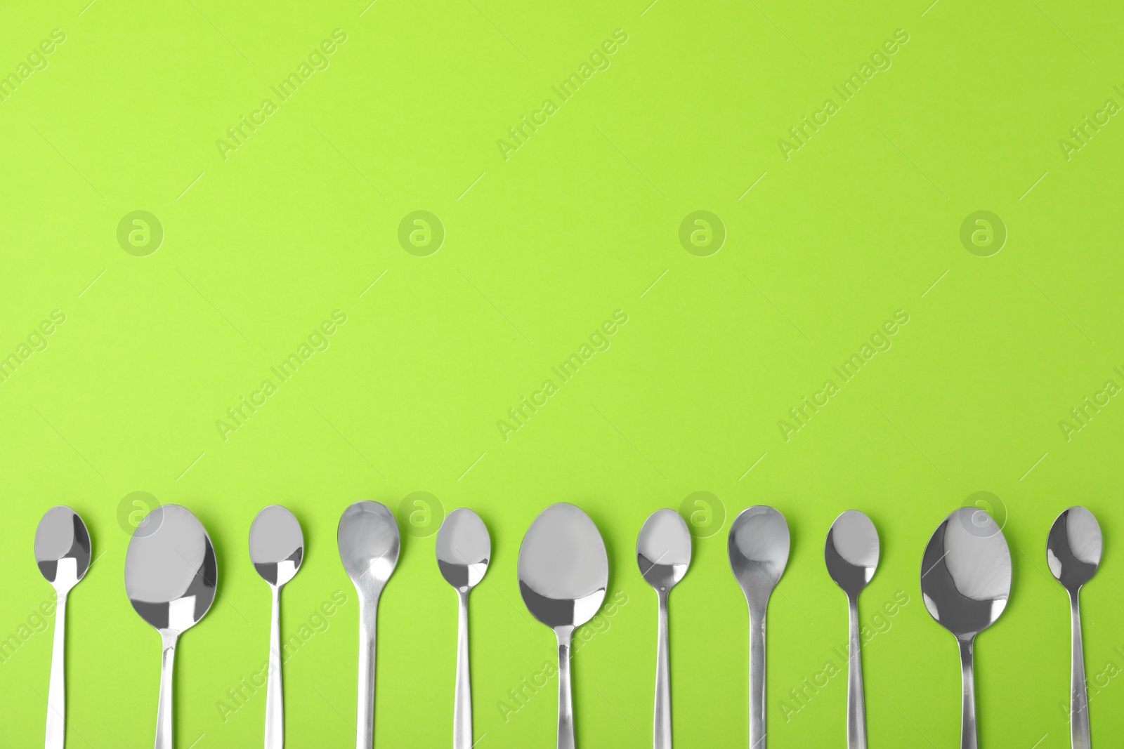 Photo of New metal spoons on green background, flat lay with space for text