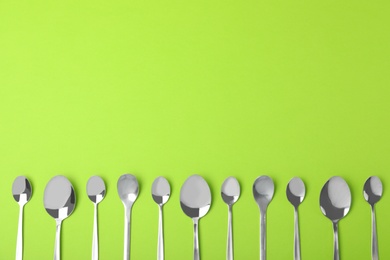 New metal spoons on green background, flat lay with space for text