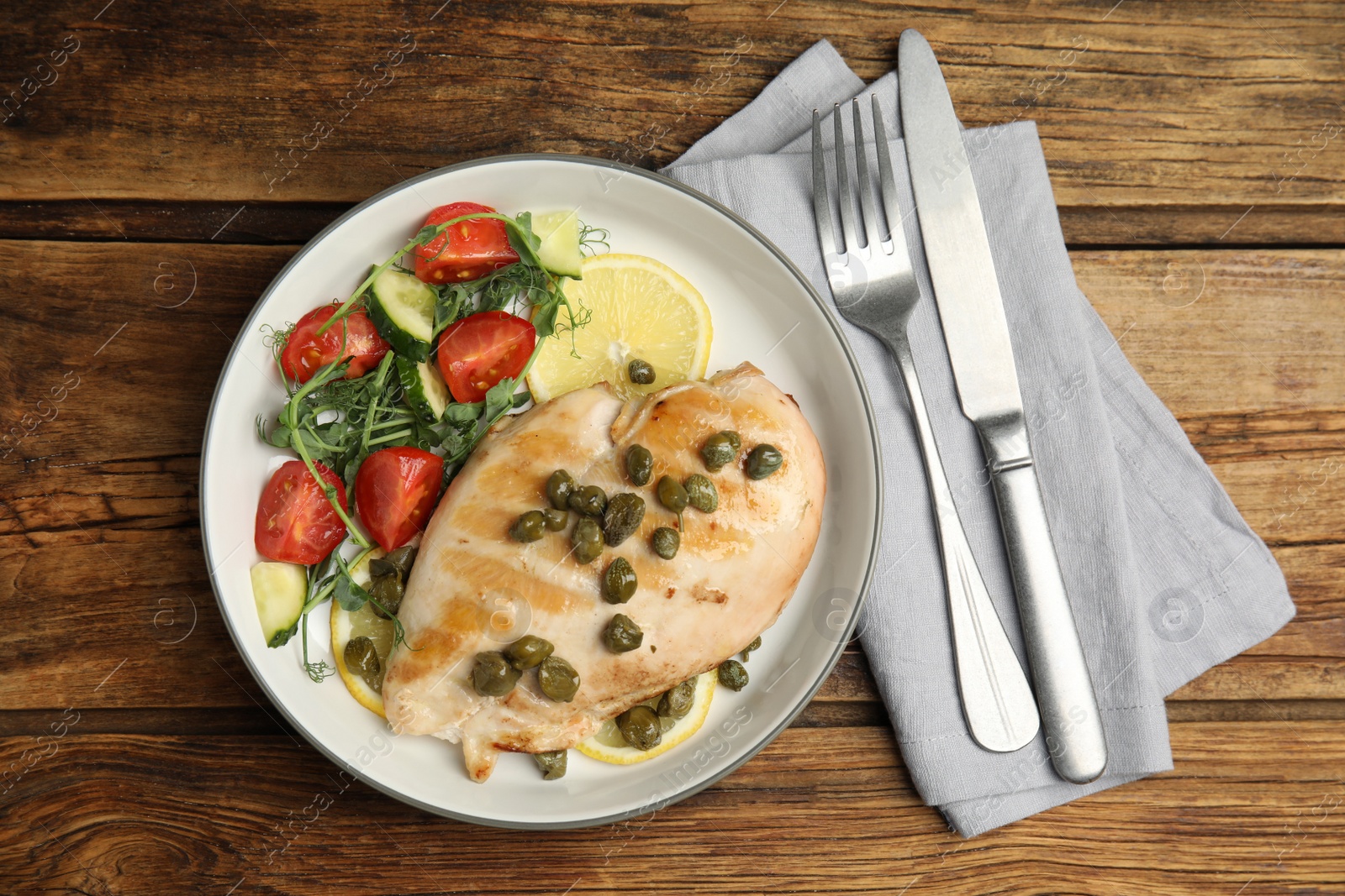 Photo of Delicious cooked chicken fillet with capers and salad served on wooden table, flat lay