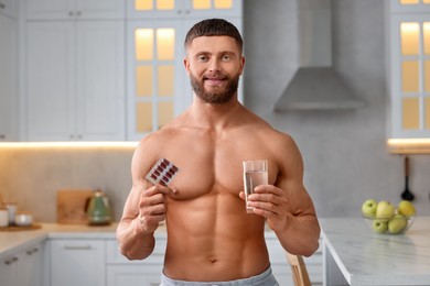 Photo of Athletic young man with pills and glass of water in kitchen. Weight loss
