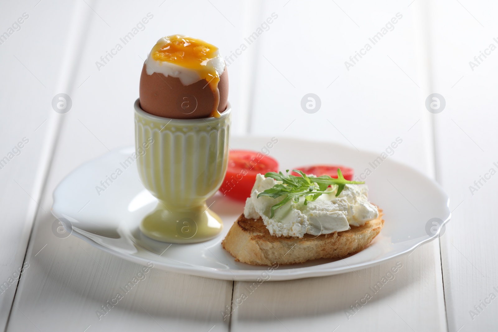 Photo of Fresh soft boiled egg in cup and sandwich served on white wooden table