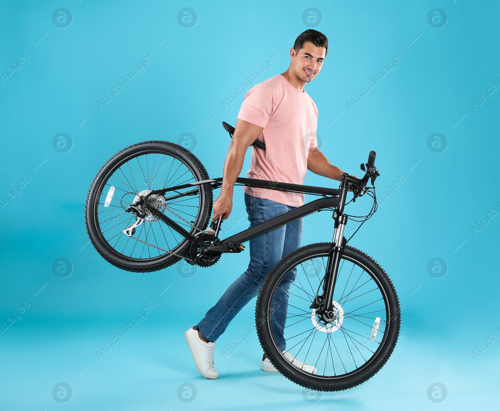 Photo of Handsome young man with modern bicycle on light blue background