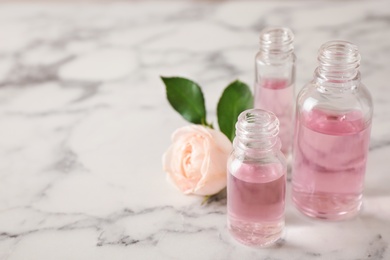 Photo of Bottles of essential oil and rose on marble table. Space for text